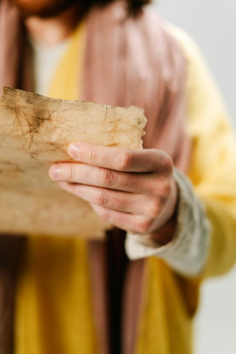 A close-up of a person in a robe holding an aged parchment scroll.