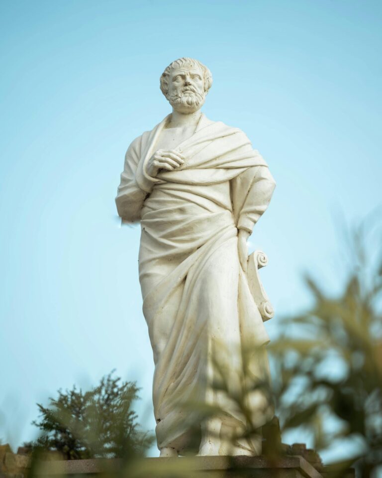 Majestic marble statue of an ancient Greek philosopher in an outdoor park setting under a clear blue sky.